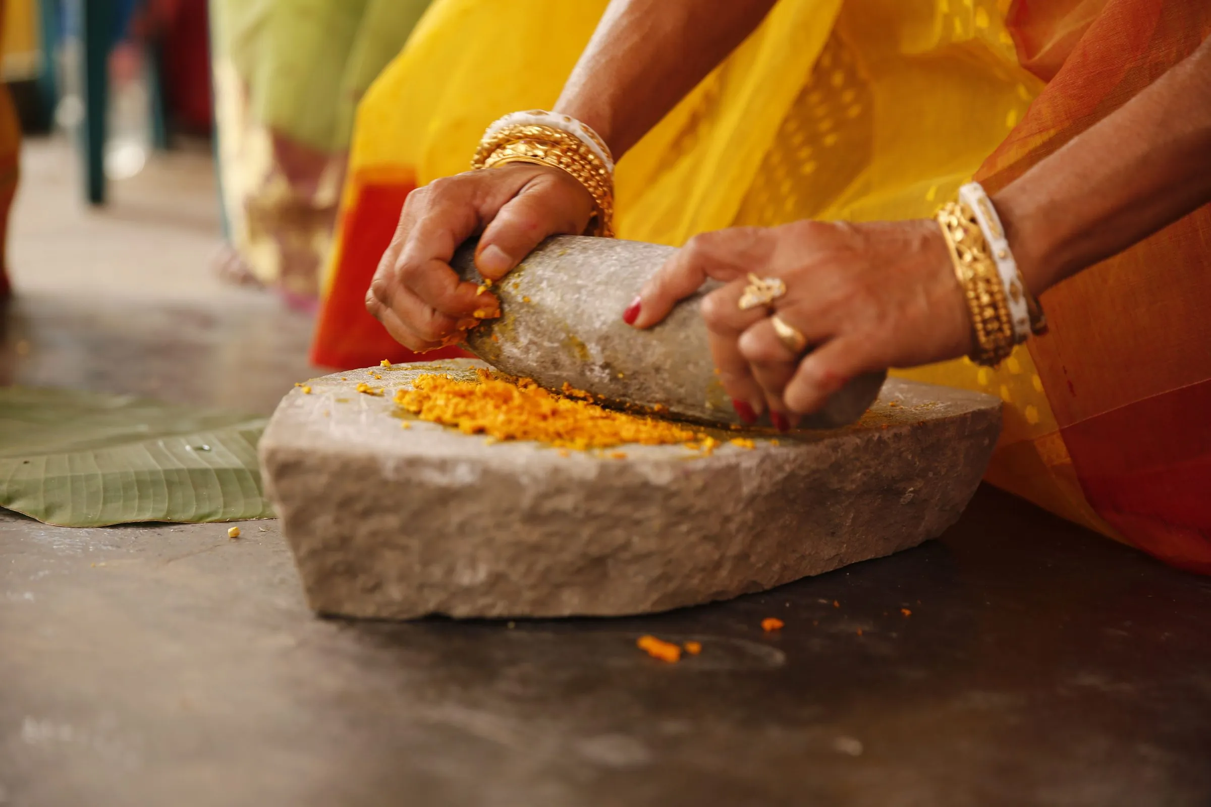 Hands grinding fresh turmeric on a stone sil batta