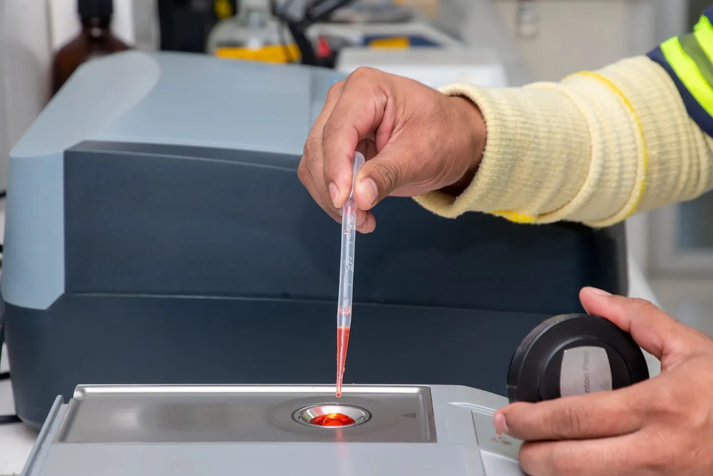 A lab technician placing a sample on an instrument with a pipette